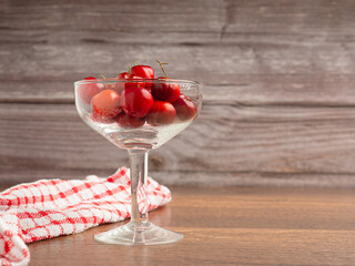 Ripe red acerola cherries in a glass on a wooden table with a wood wall background