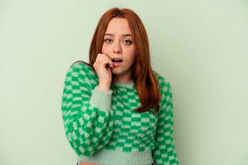 Young caucasian woman isolated on green background biting fingernails, nervous and very anxious.