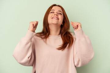 Young caucasian woman isolated on green background celebrating a victory, passion and enthusiasm, happy expression.