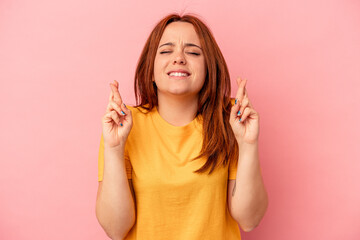 Obraz premium Young caucasian woman isolated on pink background crossing fingers for having luck