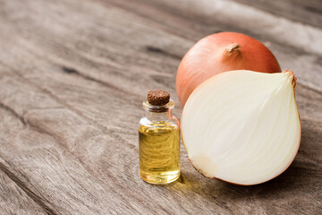 Onion oil in glass bottle and fresh onion with half sliced isolated on wooden table background. 