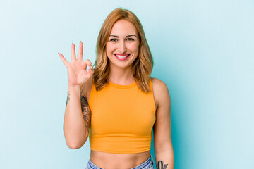 Young caucasian woman isolated on blue background cheerful and confident showing ok gesture.