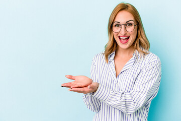 Young caucasian woman isolated on blue background holding a copy space on a palm.