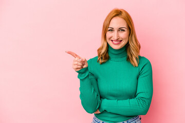 Young caucasian woman isolated on pink background smiling cheerfully pointing with forefinger away.