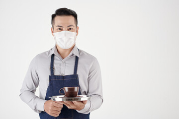Portrait of coffeeshop waiter in medical mask serving cup of freshly made coffee