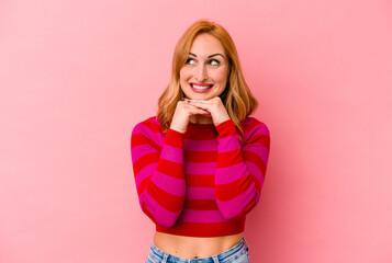 Young caucasian woman isolated on pink background keeps hands under chin, is looking happily aside.
