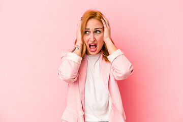 Young caucasian woman isolated on pink background covering ears with hands trying not to hear too loud sound.