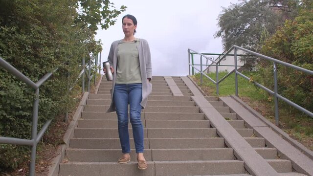A woman with thermal paint in her hands goes down the stairs of the city. The transition between levels in the city, urban studies. On the stairs there is a ramp for strollers