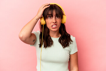 Young Argentinian woman listening to music isolated on pink background being shocked, she has remembered important meeting.