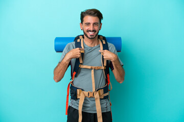 Young mountaineer man with a big backpack isolated on blue background with surprise facial expression