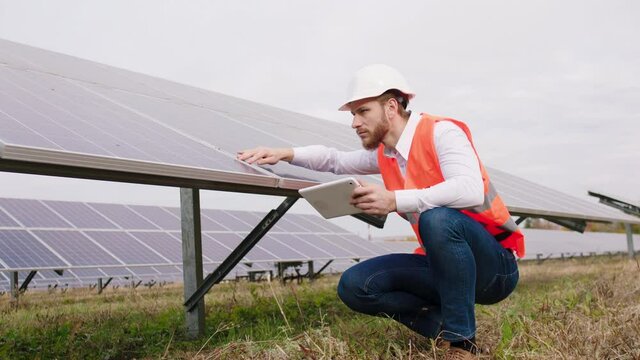 Ecological engineer man with safety helmet at solar panels farm concentrated checking the operation of sun and cleanliness of photovoltaic solar batteries