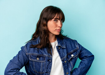 Young Argentinian woman isolated on blue background frowning face in displeasure, keeps arms folded.