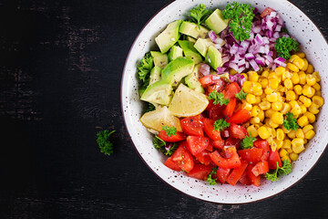 Salad with avocado, tomatoes, red onions and sweet corn in bowl. Vegetarian buddha bowl. Vegan food. Top view, flat lay