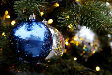 Obraz na płótnie Canvas Christmas decorations on a fir branches on festive lights background, night illumination. New Year tree with blue and silver toy balls, water drops in rainy weather
