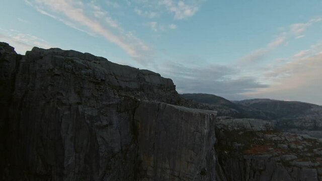 Flying close to rocky mountain side towards group of people, aerial FPV shot