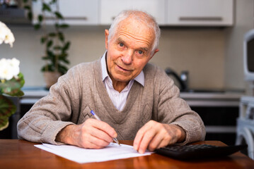 elderly pensioner writing on piece of paper at table in kitchen