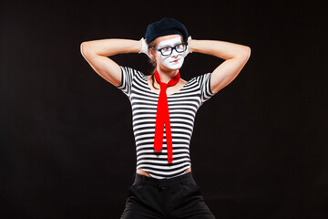 Portrait of male mime artist performing, isolated on black background. Man puts his hands behind his head. Symbol of manhood, male power