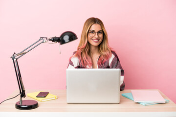 Young student woman in a workplace with a laptop over pink background keeping the arms crossed in...