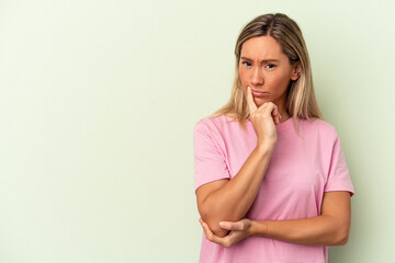 Young caucasian woman isolated on green background looking sideways with doubtful and skeptical expression.