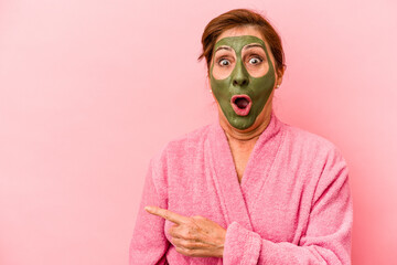 Middle age caucasian woman wearing a facial mask isolated on pink background pointing to the side