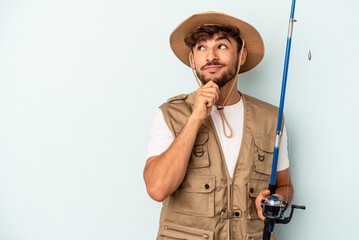 Young mixed race fisherman holding a rod isolated on blue background looking sideways with doubtful and skeptical expression.