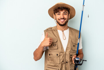 Fototapeta premium Young mixed race fisherman holding a rod isolated on blue background smiling and raising thumb up