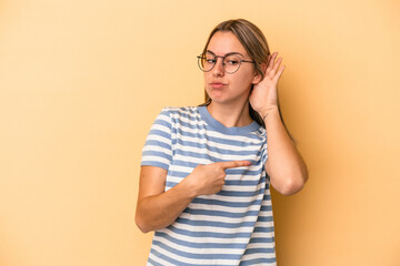 Young caucasian woman isolated on yellow background trying to listening a gossip.