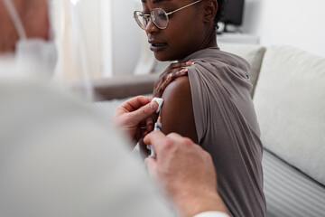 Doctor with syringe injecting covid-19 vaccine on African woman patient. Millennial female patient getting immunization against global infectious disease. Doctor preparing vaccine for young patient