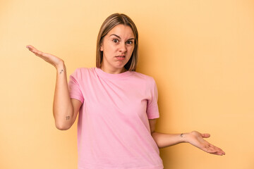 Young caucasian woman isolated on yellow background confused and doubtful shrugging shoulders to...