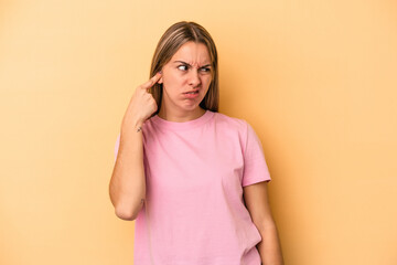 Young caucasian woman isolated on yellow background covering ears with hands.