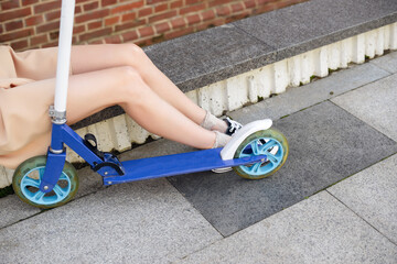 Legs of young woman and kick scooter at street.