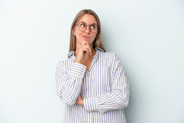 Young caucasian woman isolated on blue background thinking and looking up, being reflective, contemplating, having a fantasy.