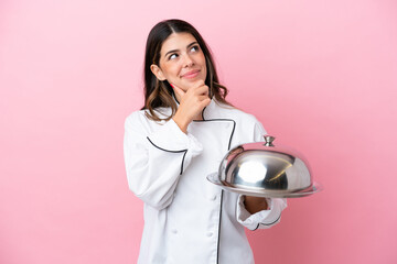 Young Italian chef woman holding tray with lid isolated on pink background and looking up