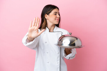 Young Italian chef woman holding tray with lid isolated on pink background making stop gesture and disappointed