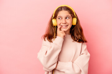 Little caucasian girl listening to music isolated on pink background relaxed thinking about something looking at a copy space.