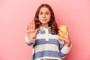 Little caucasian girl holding mobile phone isolated on pink background standing with outstretched...