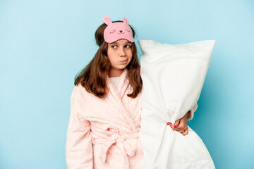 Little caucasian girl going to sleep isolated on blue background confused, feels doubtful and...