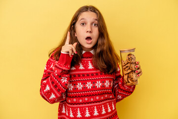 Little caucasian girl holding a Christmas cookies isolated on yellow background having an idea, inspiration concept.