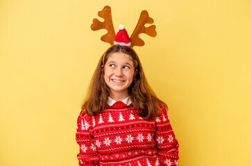 Little caucasian girl wearing a Christmas reindeer hat isolated on yellow background dreaming of achieving goals and purposes