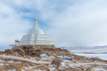 White Buddhist stupa and ritual trees with colorful ribbons on a cloudy winter day at the top of the sacred island of Ogoy. Lake Baikal, Siberia, Russia - 472030750