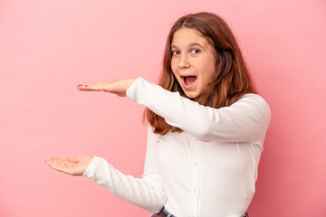 Little caucasian girl isolated on pink background shocked and amazed holding a copy space between hands.
