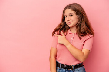 Little caucasian girl isolated on pink background smiling and pointing aside, showing something at blank space.