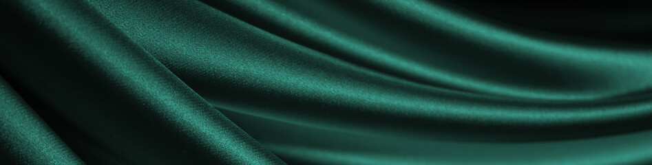 Emerald green silk satin curtain. Close-up. Soft wavy folds on shiny fabric. Elegant background...