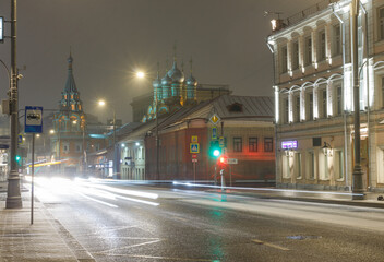 Fototapeta na wymiar Moscow, Russia, Nov 19, 2021: Night view of Bolshaya Polyanka street. Church of st. Gregory of Neocaesarea. Beginning of snowfall. Car traces