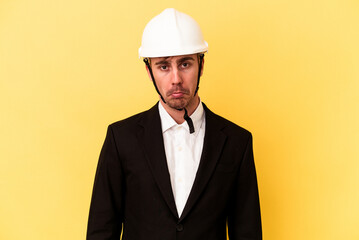 Young architect caucasian man isolated on yellow background shrugs shoulders and open eyes confused.