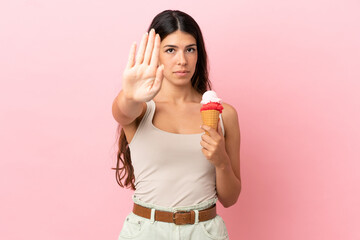 Young caucasian woman with a cornet ice cream isolated on pink background making stop gesture