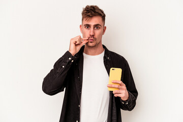 Young caucasian man holding a mobile phone isolated on white background with fingers on lips keeping a secret.