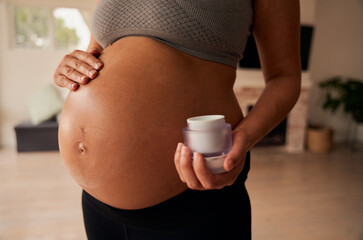 Caucasian female standing in living room rubbing moisturiser onto pregnant belly 
