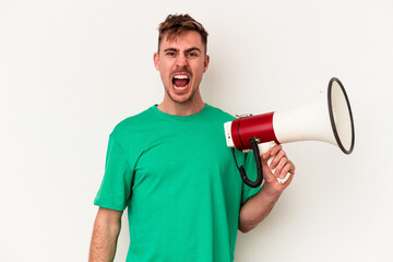 Young caucasian man holding megaphone isolated on white background screaming very angry and aggressive.