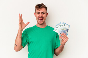 Young caucasian man holding bank notes isolated on white background receiving a pleasant surprise, excited and raising hands.